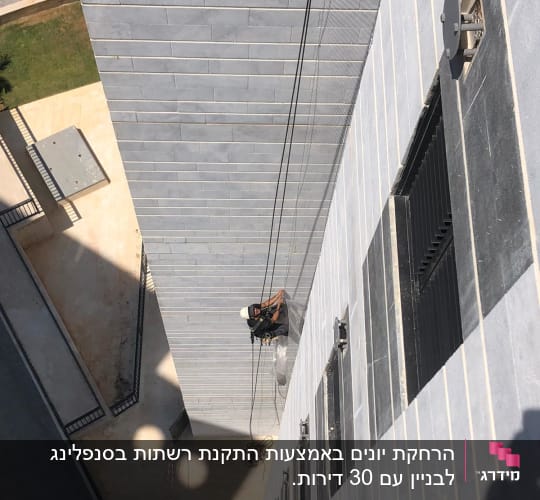 אדם על חבלים מתקין רשת על קיר בניין